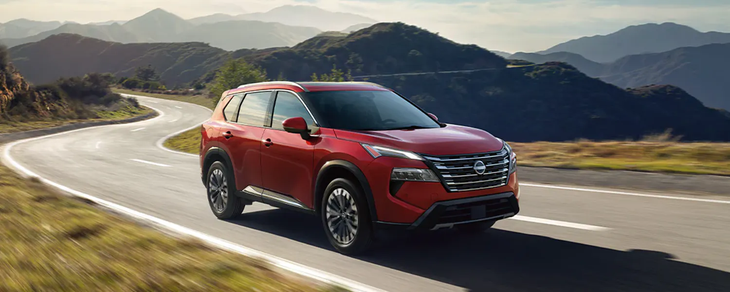 Red Nissan Rogue driving through a mountain landscape